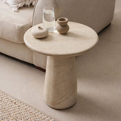 Pieces For Places Ida round lamp table in beige travertine finish with a sleek central column leg in a living room.