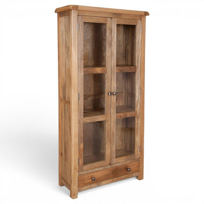 Pieces For Places Olda Glazed Display Cabinet in natural mango wood with glass doors, three shelves, and a bottom drawer.