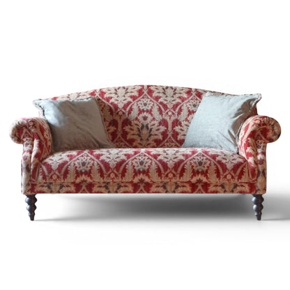 Pieces For Places Tallis Petit Sofa in red damask fabric with rolled arms and two light grey scatter cushions on dark wood legs.